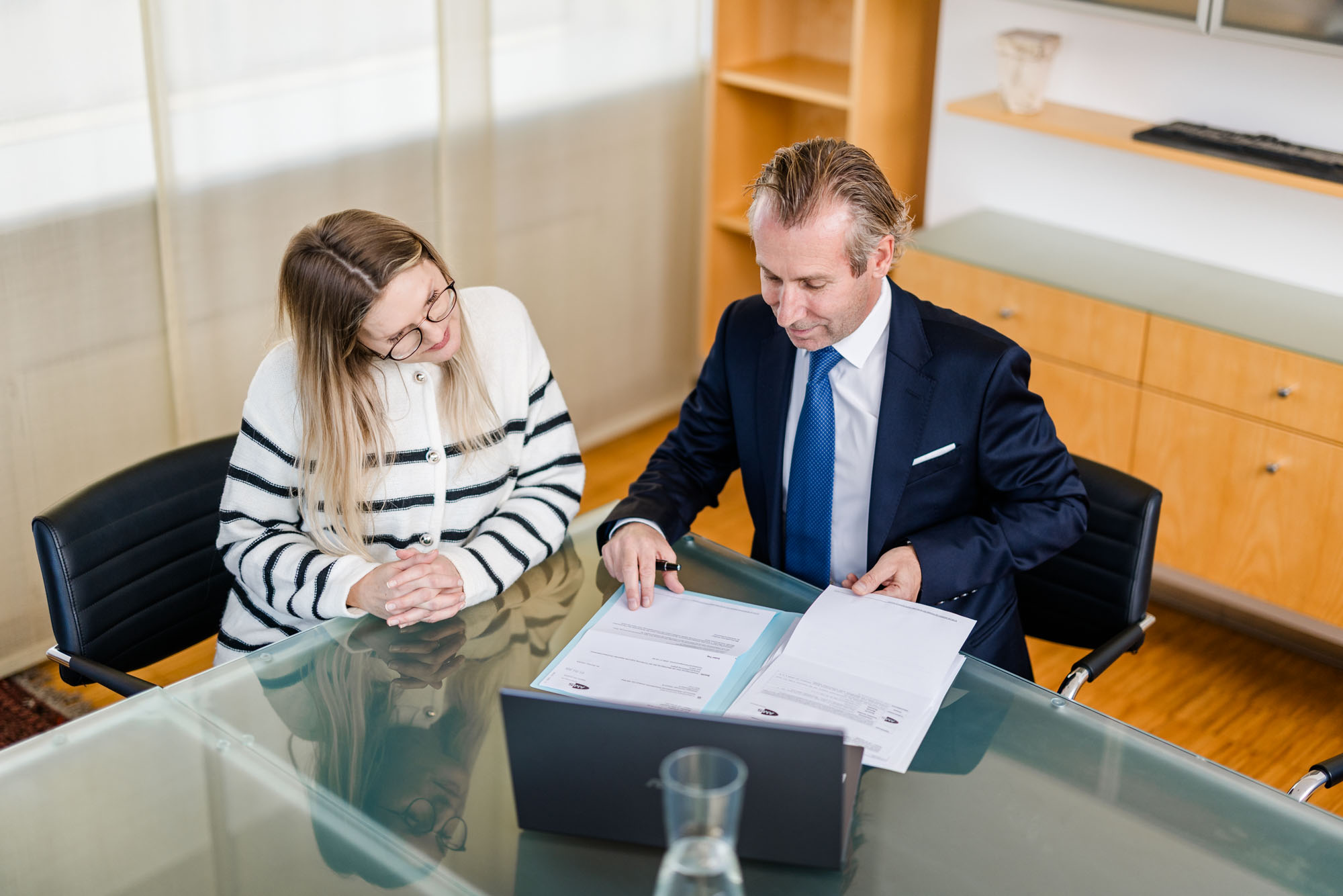 Frau und Anwalt sitzen gemeinsam an einem Tisch mit Laptop und Unterlagen