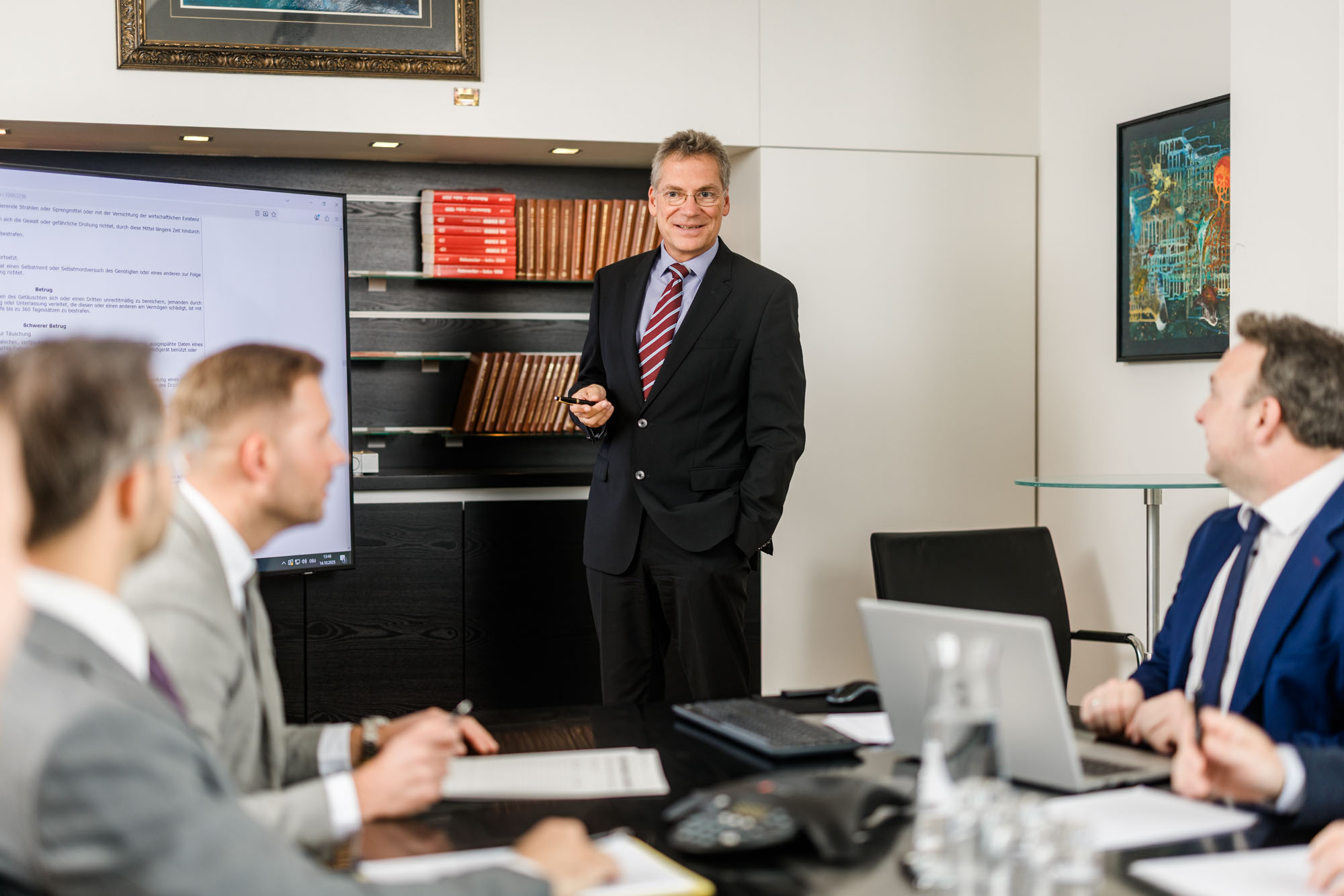 Mann im Anzug steht vor einem Bildschirm und präsentiert etwas