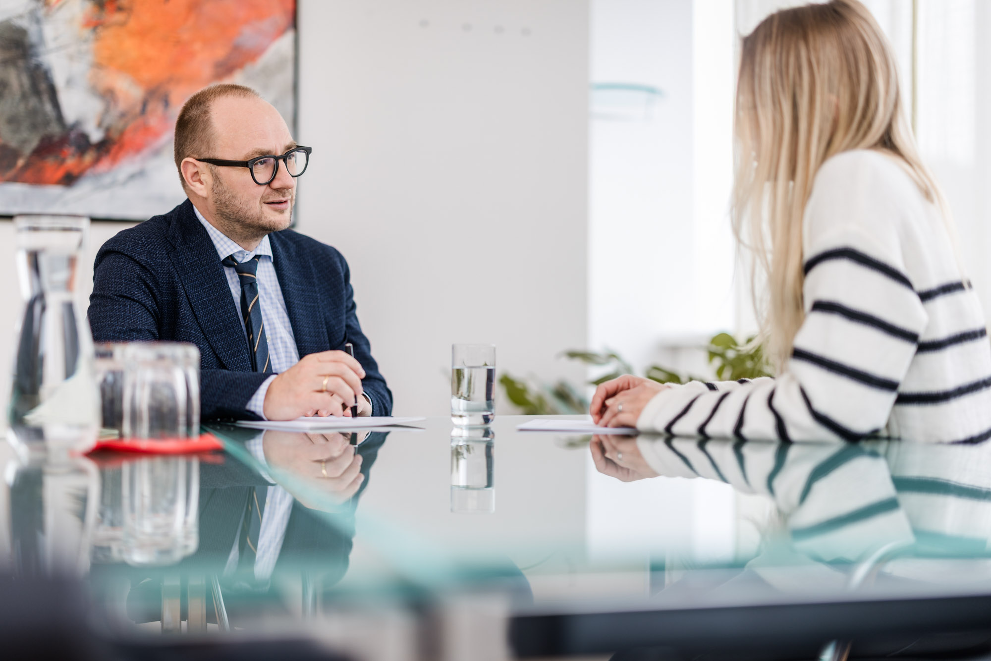 Anwalt und Dame sitzen an einem Glastisch und führen ein Gespräch.