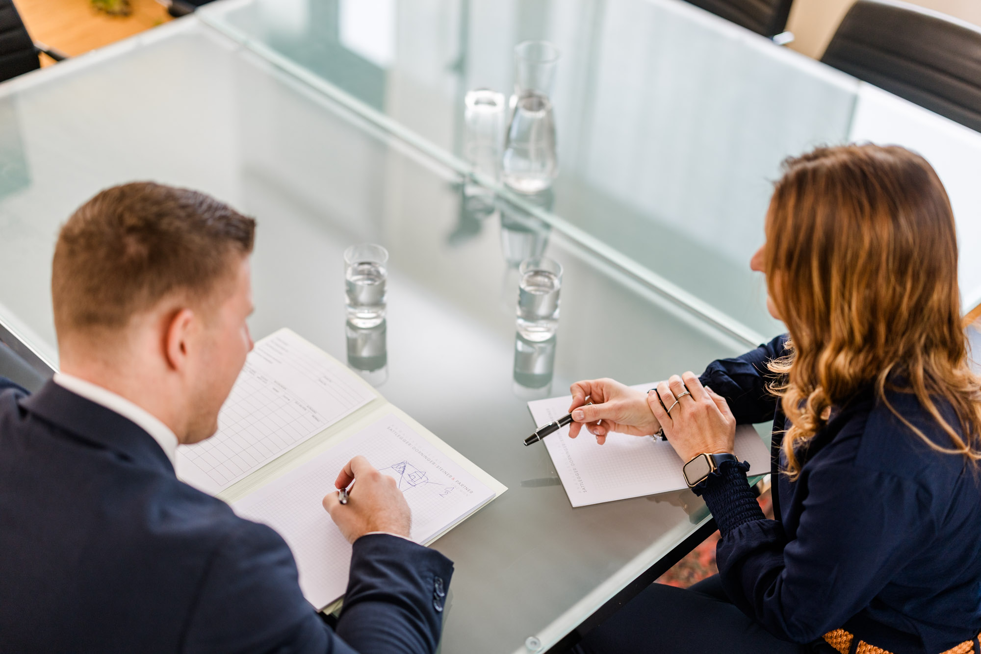 Ansicht von oben auf zwei Personen die etwas auf einem Dokument besprechen.